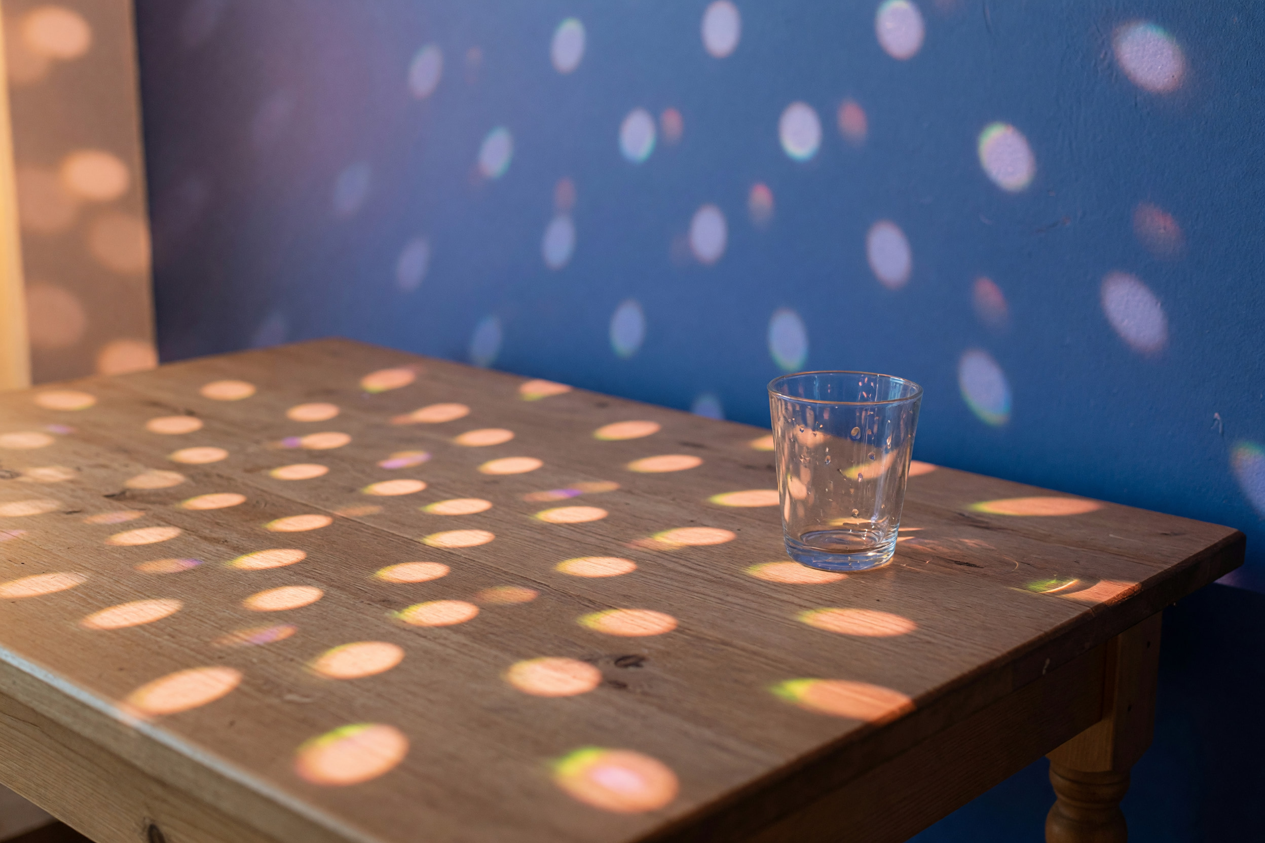 Gedeckter Holztisch im Gastraum mit gestreuten Discokugel-Lichtpunkten vor kobaltblauer Wand