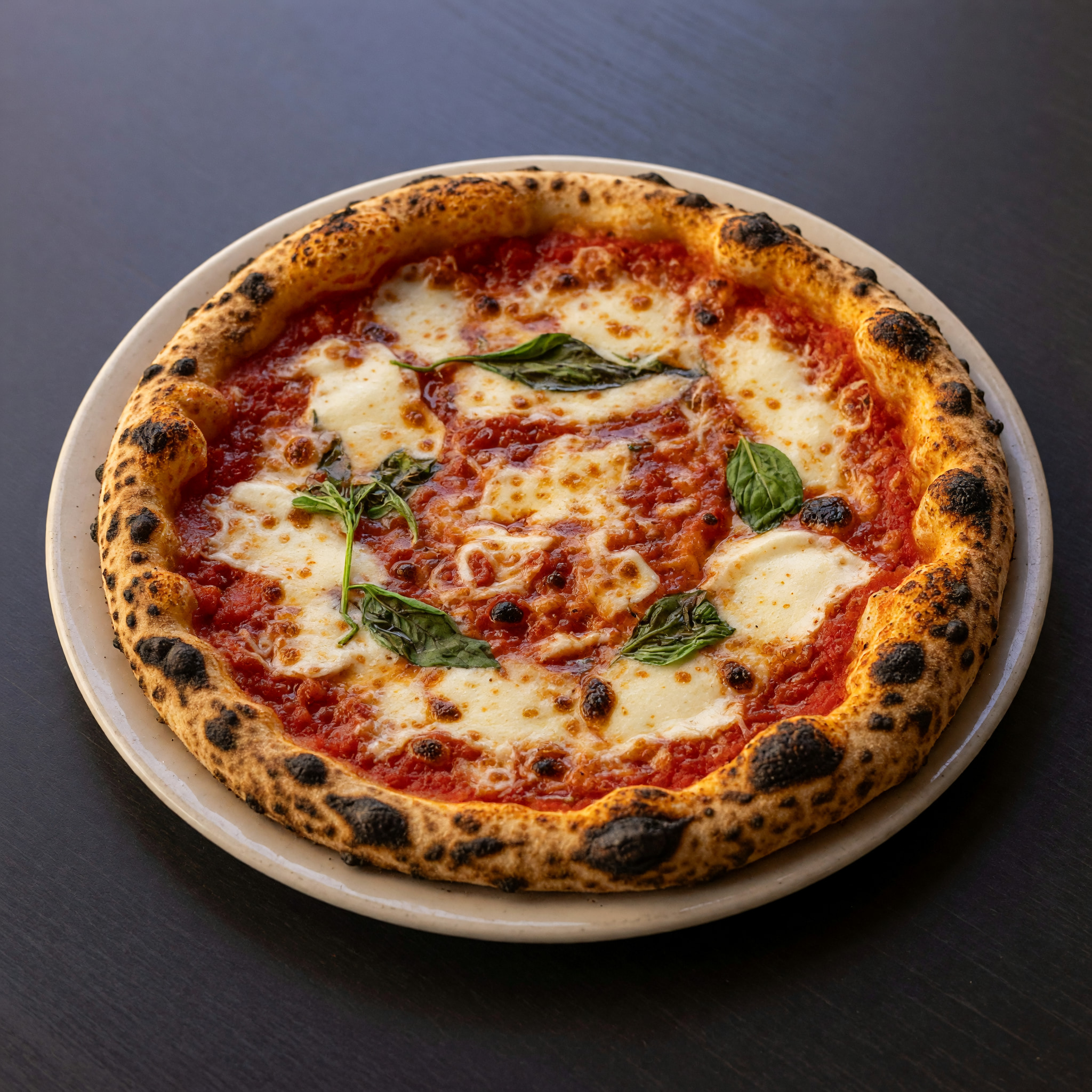 Neapolitanische Pizza mit geröstetem Rand, geschmolzenem Mozzarella, Tomatensauce und Basilikum auf hellem Teller